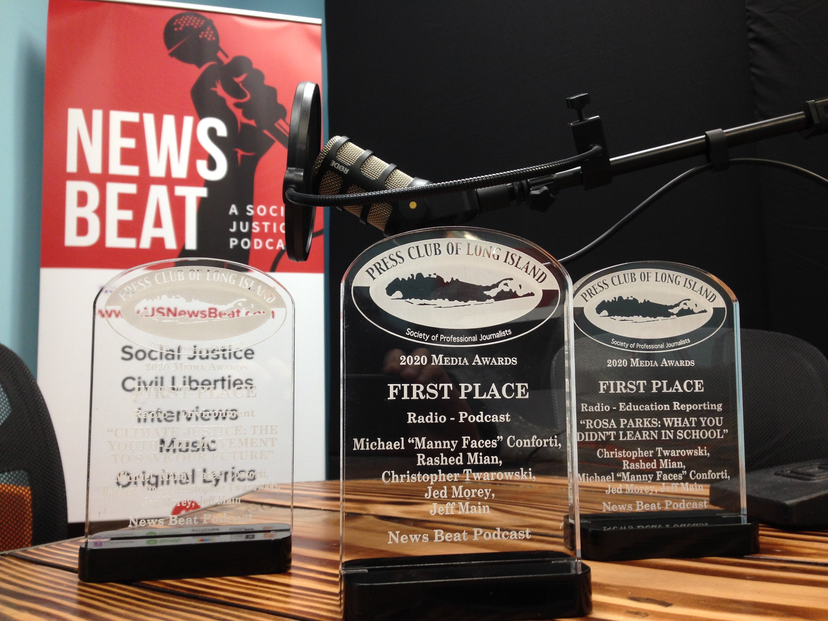 Image of three First Place awards for News Beat podcast in front of a microphone and logo banner