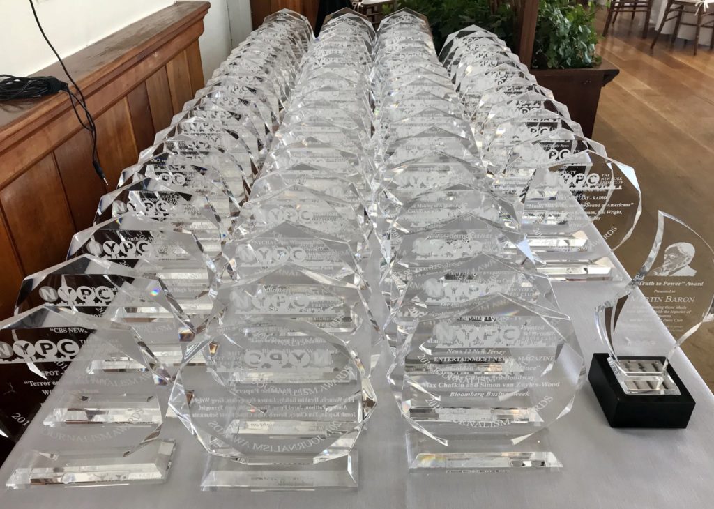 Dozens of Crystal New York Press Club Journalism Awards Arranged Across a Table