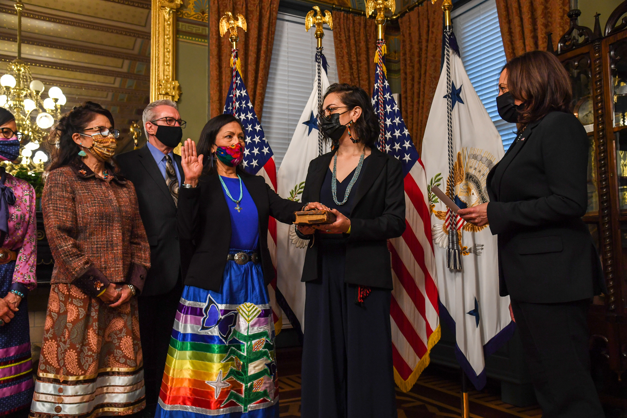 Interior Secretary Deb Haaland is being swrong in to her new position. She has a hand raised and is facing Vice President Kamala Harris. 